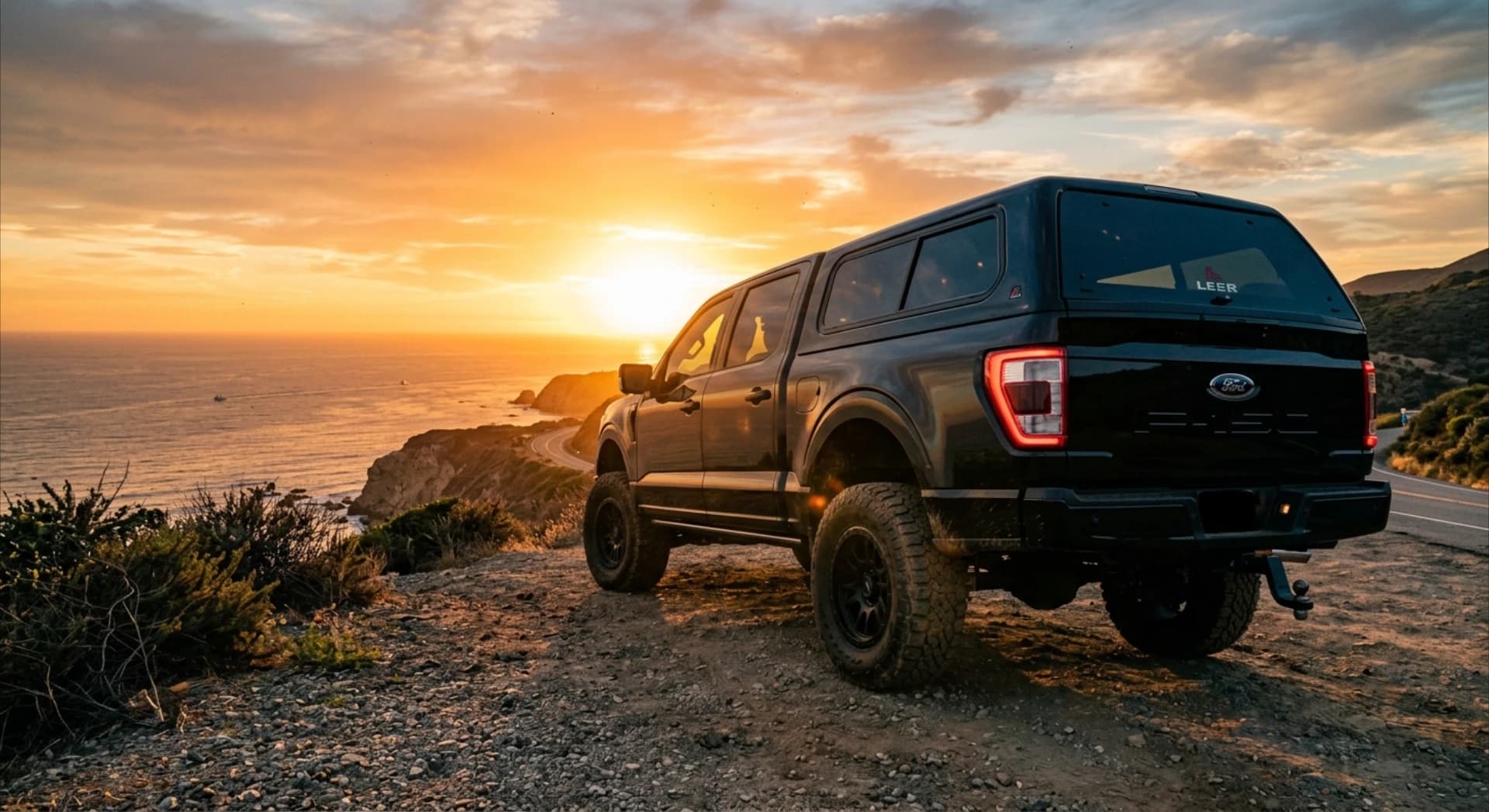 Black Ford F-150 fitted with a LEER truck cap, parked on a coastal overlook at sunset