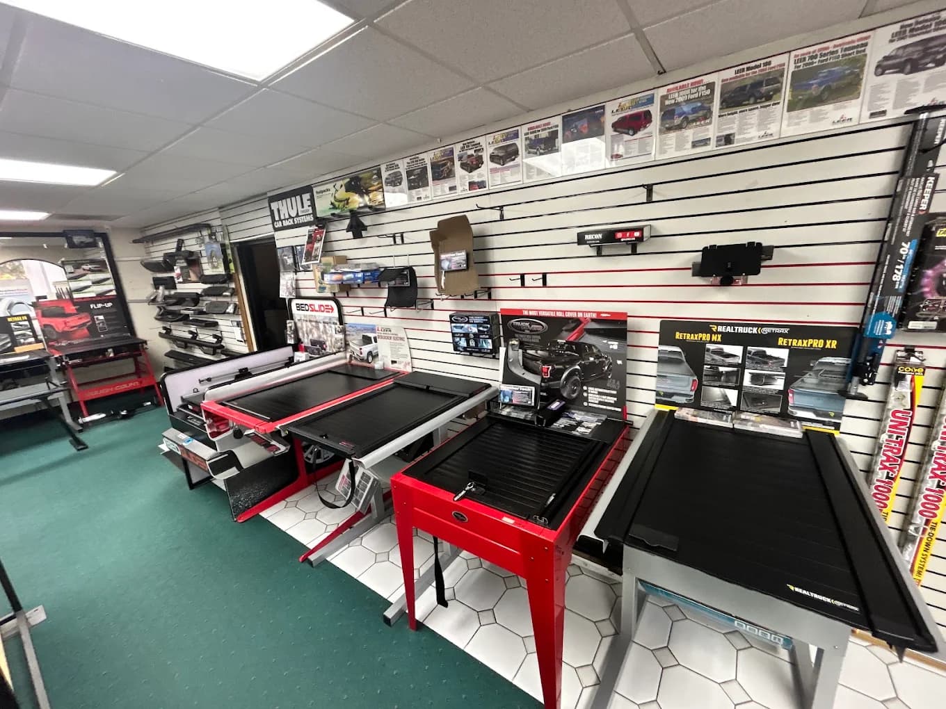 Retractable and folding tonneau covers displayed on stands beside a slatwall of LEER product literature