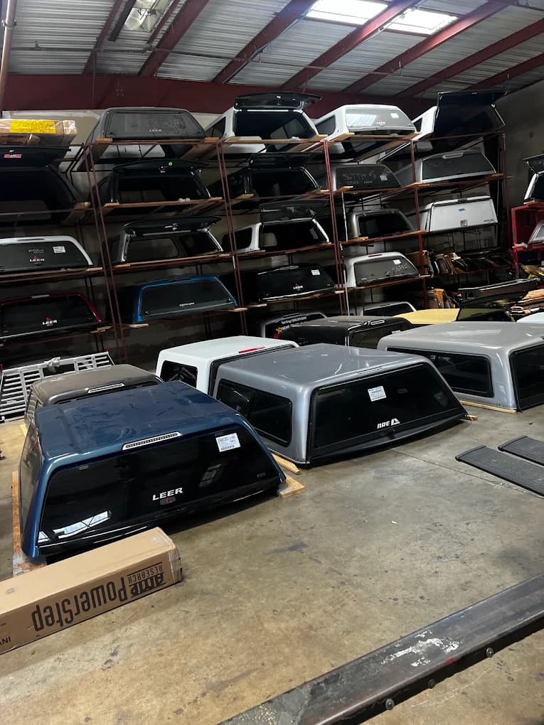 Truck caps stacked on multi-level warehouse racks, with LEER and A.R.E. shells in the foreground