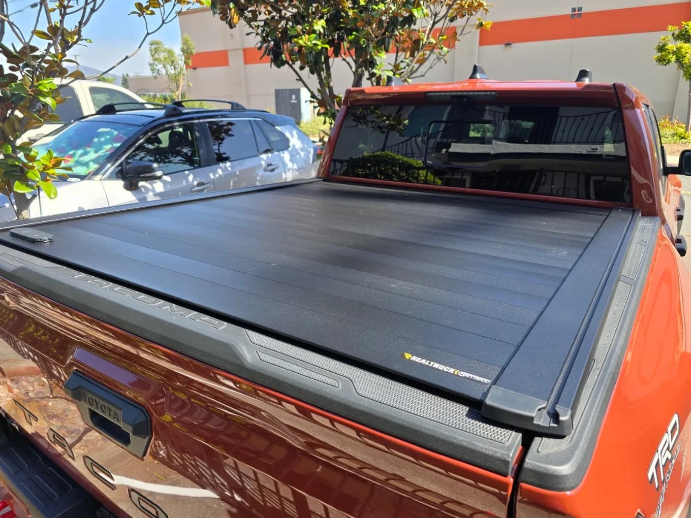 Orange Toyota Tacoma with a black retractable hard tonneau cover closed over the bed