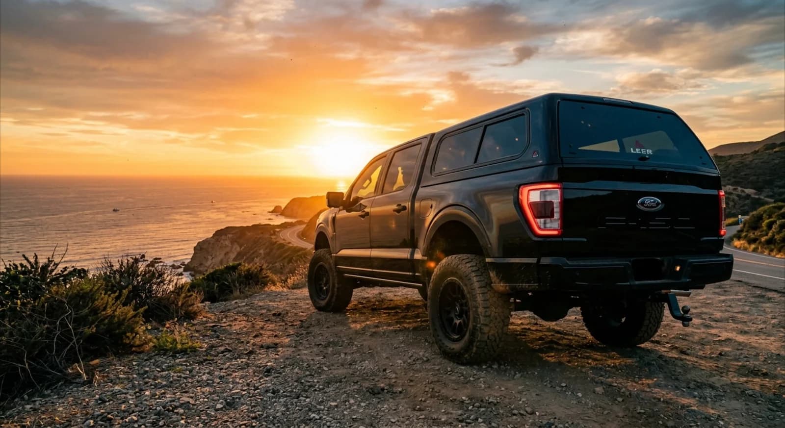 Black Ford F-150 with a LEER truck cap parked on a coastal overlook in San Diego at sunset
